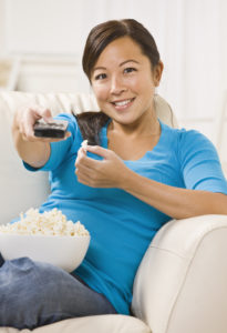 Woman siting on a couch pointing a remote control.