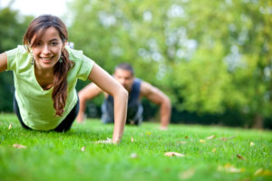 Woman and man are doing push ups in on grass.